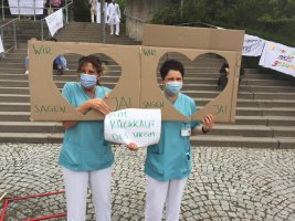 Protest 2020 in Gießen: zwei Personen im Kasack schauen durch zwei in einen Karton geschnittene Löcher in Herzsymbolform: »Wir sagen ja zum Rückkauf des UKGM«