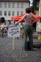 Protest 2020 in Gießen: eine Person steht breitbeinig neben ihr ein Schild: »UKGM zurück zum Land«, im Hintergrund spricht jemand